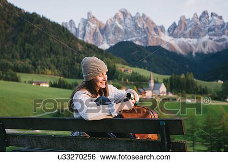 Stock Photograph - Woman relaxing on park bench, Santa Maddalena, Dolomite Alps, Val di Funes (Funes Valley), South Tyrol, Italy. Fotosearch