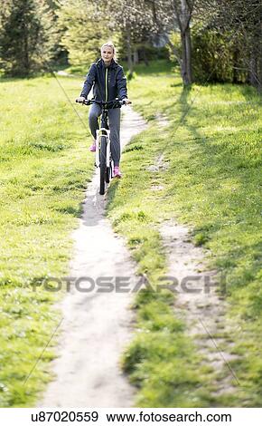 Stock Photo - Woman riding bicycle on dirt track. Fotosearch