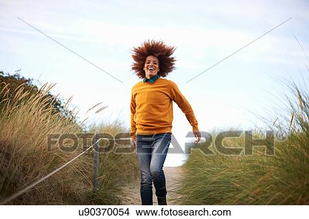 Picture - Woman running down grassy dune. Fotosearch