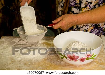 Stock Photo - Woman sieving flour at table, mid section. Fotosearch