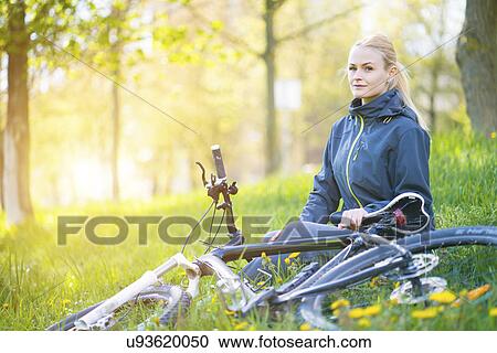 Stock Image - Woman sitting in woods with bicycle. Fotosearch