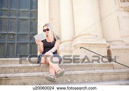 Picture - Woman using digital tablet on steps, Lecce, Italy. Fotosearch