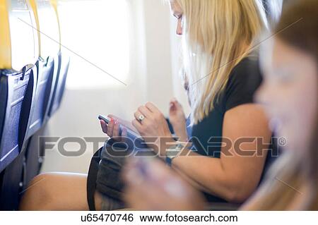 Stock Photograph - Woman using mobile phone in airplane. Fotosearch