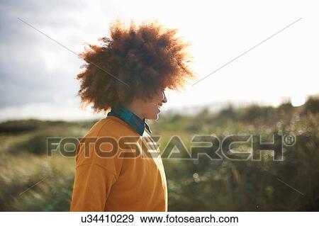 Stock Photo - Woman with afro hair on grassy dune. Fotosearch