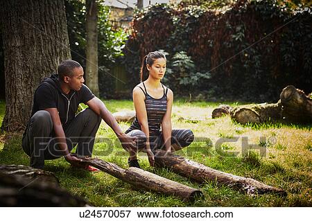 Woman with personal trainer crouching to lift tree trunk in park View Large Photo Image Stock Photo - Woman with personal trainer crouching to lift tree trunk in park. Fotosearch