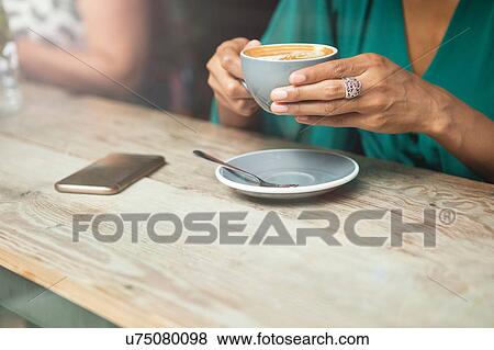Stock Photo - Woman's hands holding coffee cup in cafe window. Fotosearch