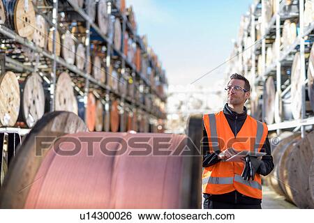 Stock Photograph - Worker inspecting cable reels with digital pad at cable storage facility. Fotosearch