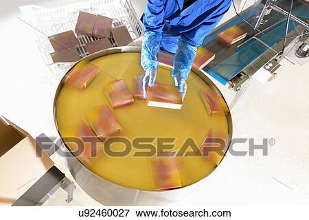 Stock Photo - Worker on packaging line in Asian food factory. Fotosearch