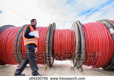 Stock Photography - Worker walking past reels of electrical cable at cable storage facility. Fotosearch