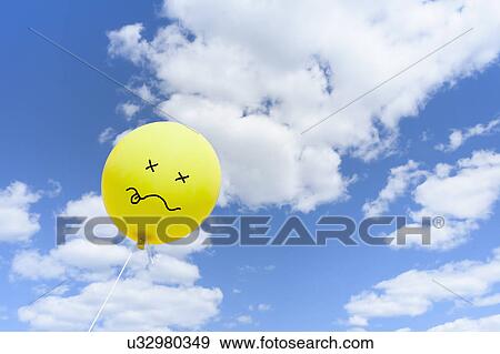 Stock Photo - Yellow balloon with drawn face against blue sky. Fotosearch