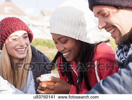 Stock Image - Young adult friends crouching on beach with coffee takeaway, Western Cape, South Africa. Fotosearch