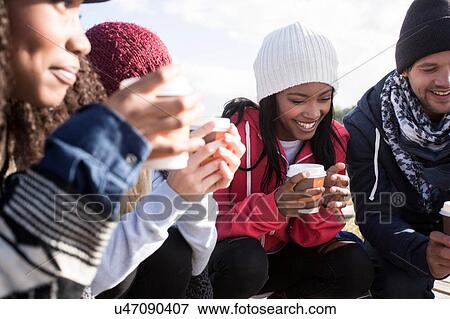 Stock Photo - Young adult friends crouching on beach with coffee takeaway, Western Cape, South Africa. Fotosearch