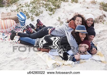 Stock Image - Young adult friends lying on top of each other having fun at beach, Western Cape, South Africa. Fotosearch