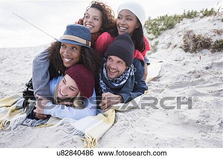 Stock Photograph - Young adult friends lying on top of each other on picnic blanket at beach, Western Cape, South Africa. Fotosearch