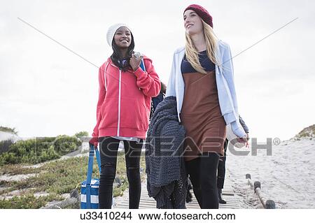 Picture - Young adult picnicking friends strolling on boardwalk at beach, Western Cape, South Africa. Fotosearch