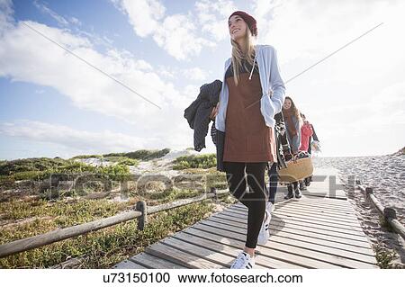 Stock Image - Young adult picnicking friends strolling along beach boardwalk, Western Cape, South Africa. Fotosearch