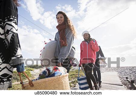 Stock Image - Young adult picnicking friends strolling along beach boardwalk, Western Cape, South Africa. Fotosearch