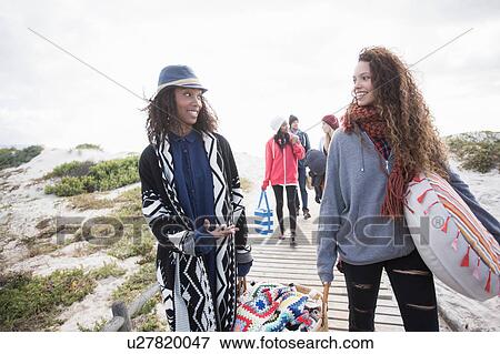 Stock Photo - Young adult picnicking friends strolling on beach boardwalk, Western Cape, South Africa. Fotosearch