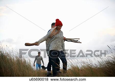 Stock Photo - Young adults collecting driftwood in coastal dunes. Fotosearch