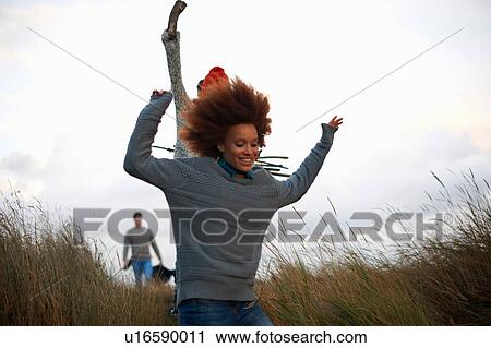 Stock Image - Young adults running in coastal dunes. Fotosearch