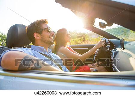 Stock Image - Young couple driving on sunlit rural road in convertible, Majorca, Spain. Fotosearch