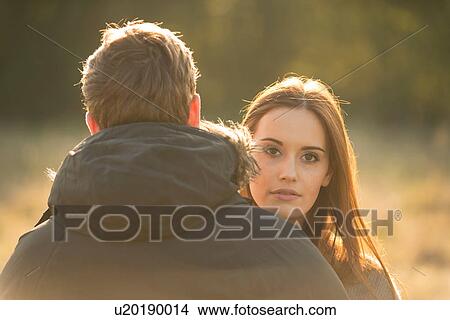 Picture - Young couple in field, young woman looking over man's shoulder. Fotosearch