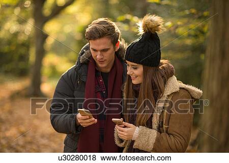 Young couple in forest, looking at smartphones View Large Photo Image Stock Photo - Young couple in forest, looking at smartphones. Fotosearch