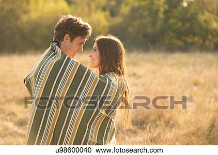 Young couple in rural setting, wrapped in blanket, face to face, smiling View Large Photo Image Stock Image - Young couple in rural setting, wrapped in blanket, face to face, smiling. Fotosearch