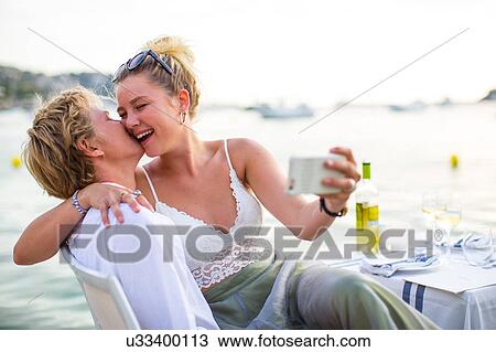 Stock Image - Young couple laughing and taking selfie at waterfront restaurant, Majorca, Spain. Fotosearch