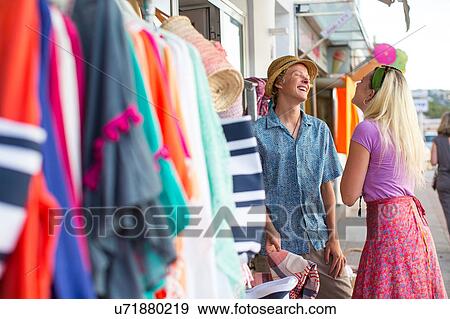 Stock Photo - Young couple laughing trying sunhat at shop front, Majorca, Spain. Fotosearch