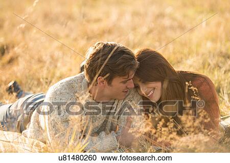 Stock Image - Young couple lying in field, smiling. Fotosearch