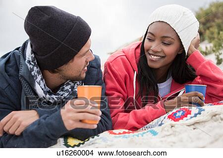 Picture - Young couple picnicking and chatting on beach, Western Cape, South Africa. Fotosearch