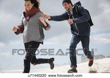 Stock Image - Young couple running and chasing on beach, Western Cape, South Africa. Fotosearch