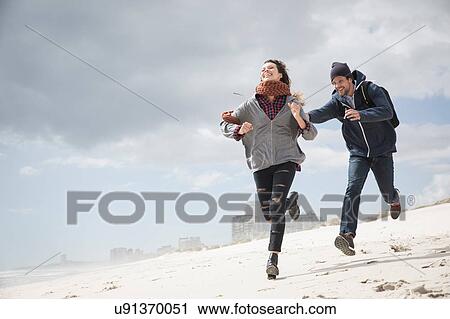 Stock Image - Young couple running and chasing on beach, Western Cape, South Africa. Fotosearch