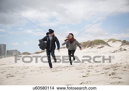 Picture - Young couple running on windswept beach, Western Cape, South Africa. Fotosearch