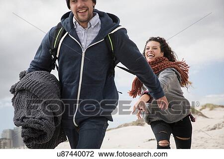 Stock Image - Young couple running on windswept beach, Western Cape, South Africa. Fotosearch