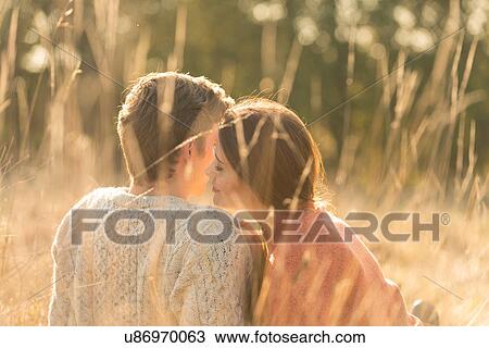 Stock Image - Young couple sitting in rural setting, kissing. Fotosearch