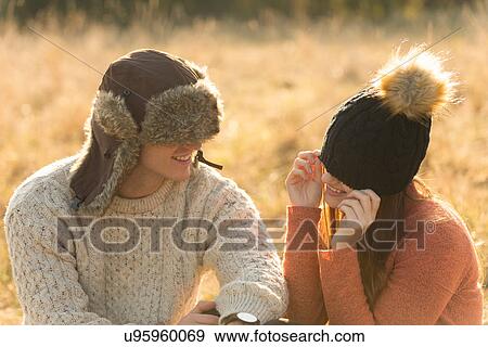 Stock Photo - Young couple sitting in rural setting, wearing warm hats. Fotosearch