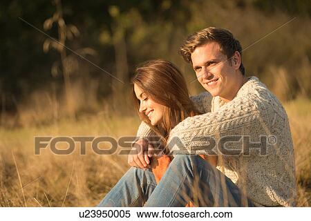 Stock Photography - Young couple sitting in rural setting, smiling. Fotosearch
