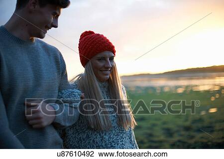 Stock Image - Young couple strolling along seaside at sunset. Fotosearch