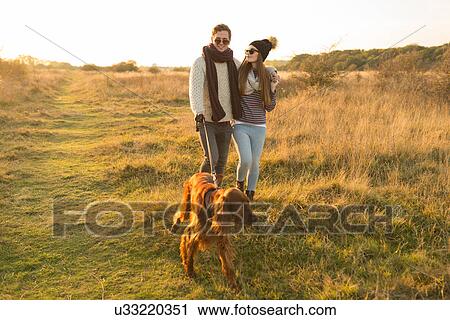 Young couple walking dog in field View Large Photo Image Stock Image - Young couple walking dog in field. Fotosearch