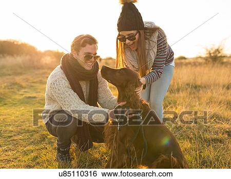 Stock Photograph - Young couple walking dog in field. Fotosearch