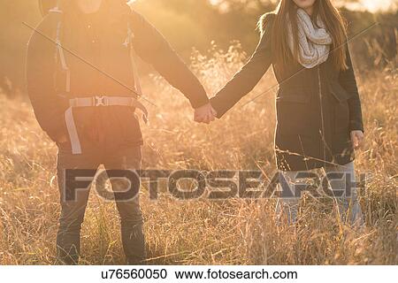 Stock Image - Young couple walking through field, holding hands, mid section. Fotosearch