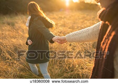 Stock Photo - Young couple walking through field, holding hands. Fotosearch