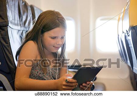 Stock Image - Young girl using digital tablet in airplane. Fotosearch