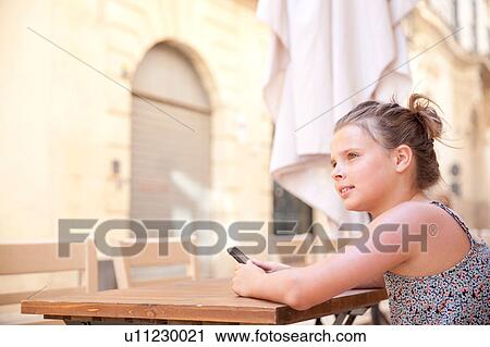 Stock Image - Young girl using mobile phone at table, Lecce, Italy. Fotosearch