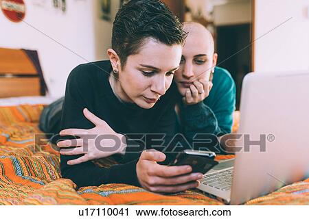 Young lesbian couple lying on bed reading smartphone texts View Large Photo Image Stock Image - Young lesbian couple lying on bed reading smartphone texts. Fotosearch