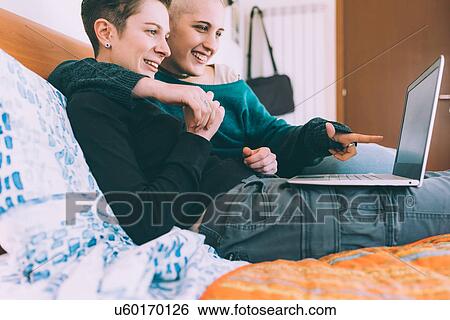 Young lesbian couple reclining on bed pointing at laptop View Large Photo Image Stock Photograph - Young lesbian couple reclining on bed pointing at laptop. Fotosearch