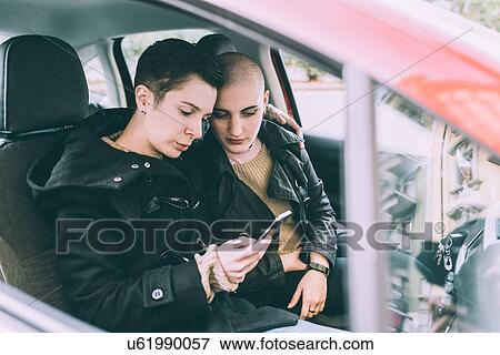 Young lesbian couple sitting in car reading smartphone texts View Large Photo Image Stock Photo - Young lesbian couple sitting in car reading smartphone texts. Fotosearch