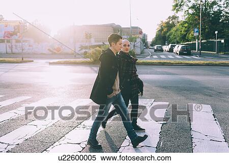 Stock Photography - Young lesbian couple walking across pelican crossing city street. Fotosearch